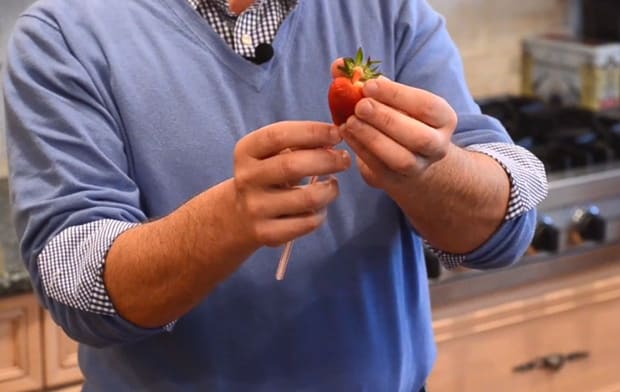 Person removing leaves off a strawberry using a straw