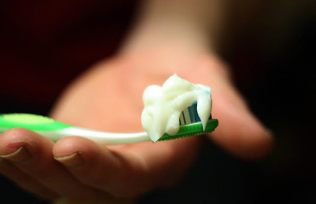 Close up of a person's hand holding a toothbrush with toothpaste on it